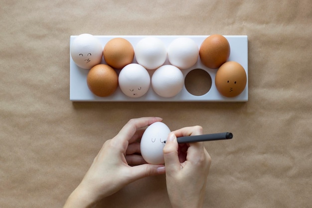 Foto las manos pintan una cara linda en los huevos de gallina en un fondo de papel marrón concepto para la vista superior de pascua