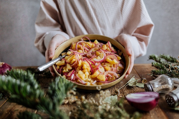 En manos de un plato grande redondo con ensalada de patatas.