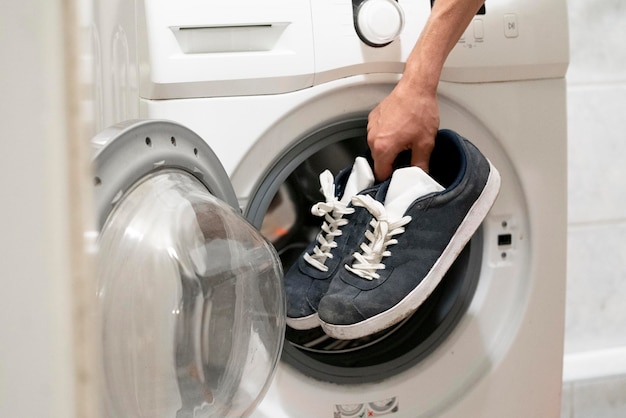 Las manos ponen las zapatillas sucias en la lavadora