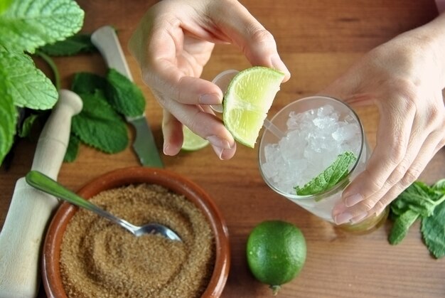 Manos preparando mojito coctel con limas y menta.