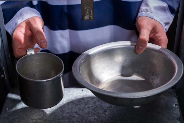 Foto las manos del preso sosteniendo platos de aluminio en un agujero para suministrar alimentos en una celda de la cárcel