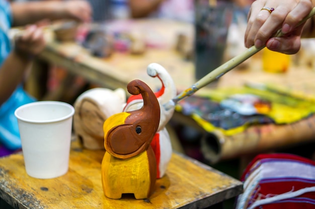 Las manos del primer de los estudiantes de arte que sostienen la brocha estudian y aprenden pintura en la muñeca animal de madera en el aula de arte.