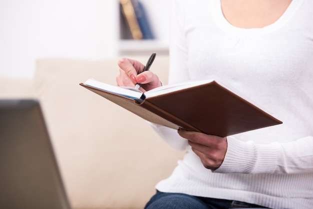 Las manos del primer de la mujer joven están escribiendo en cuaderno.