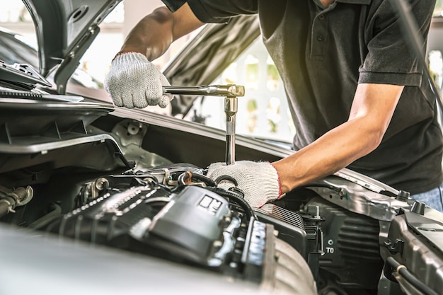 Manos de primer plano de mecánico de automóviles están utilizando la llave para reparar el motor de un automóvil.