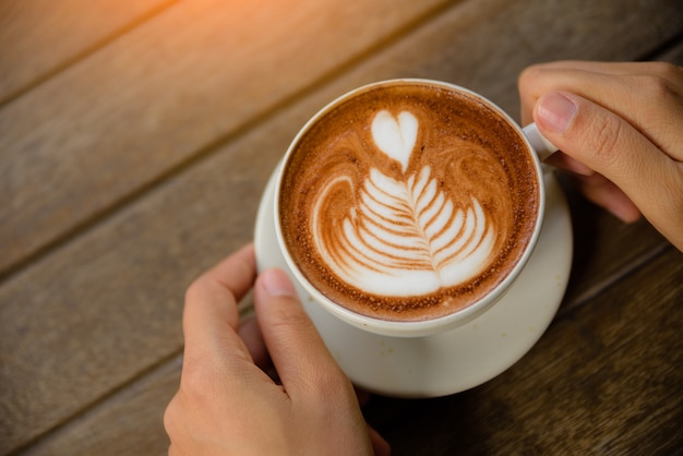 Manos que sostienen la taza de café caliente café con leche capuchino con forma de corazón. Amor, boda, valenti