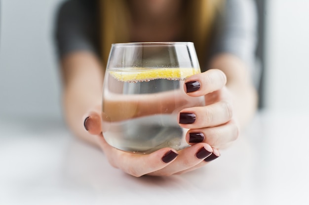 Foto manos que sostienen un vaso de agua clara con limón.