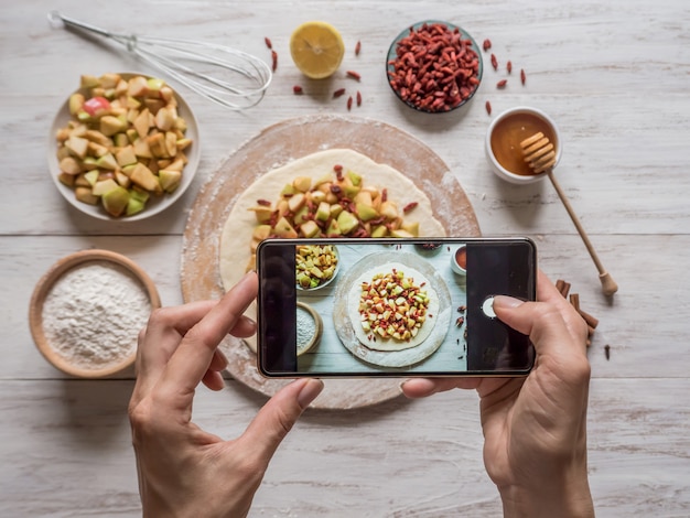 Manos que toman la foto del teléfono de la comida. Tarta de manzana para las vacaciones. Pastel con bayas de Goji y manzanas.