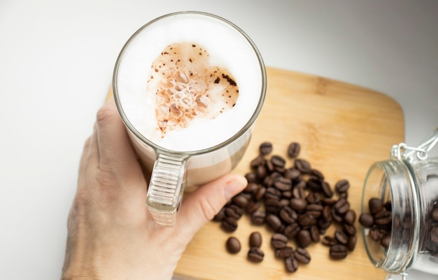 Manos recortadas de mujer sosteniendo capuchino sobre fondo blanco.