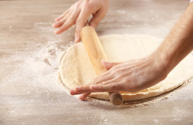 Manos rodando masa para pizza en la mesa de madera, primer plano