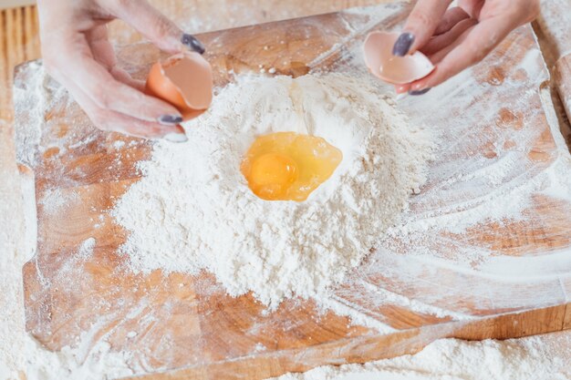 Manos rompiendo el huevo de gallina en harina sobre la mesa