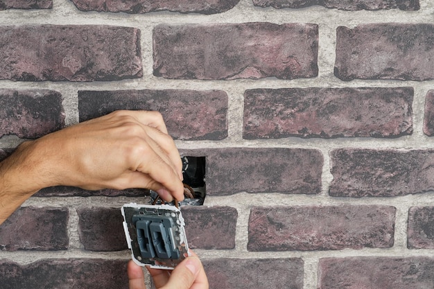 Manos sacando un interruptor de la pared para arreglarlo sosteniéndolo por los cables