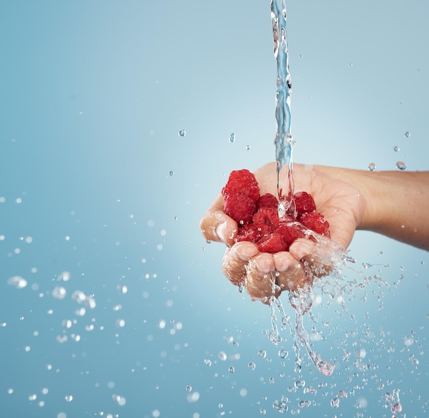 Manos con salpicaduras de agua de frambuesa y maqueta de estudio sobre fondo azul de la sostenibilidad de la fruta de verano estilo de vida saludable y nutrición de desintoxicación y vitamina c Vegano limpio y dieta bayas rojas en la palma