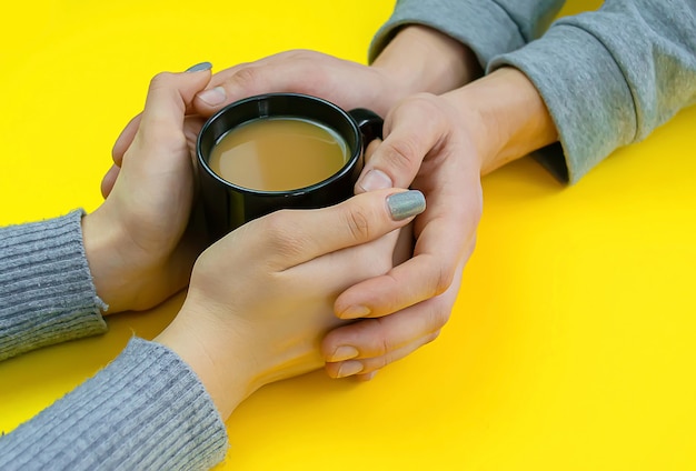 Manos sobre una mesa amarilla con café, amor. Café con leche, taza negra.