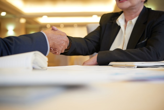 Manos de socios comerciales senior estrecharme la mano sobre la mesa del restaurante después de una reunión exitosa