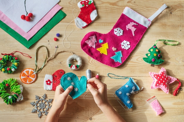 Manos sosteniendo la aguja y coser el corazón de fieltro para la decoración de navidad y año nuevo