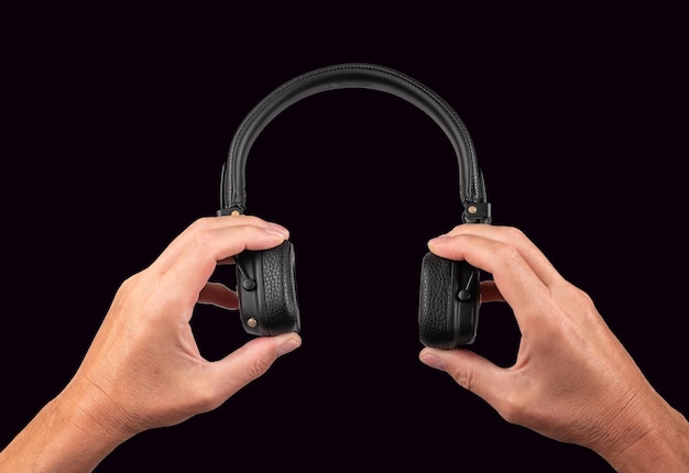 Manos sosteniendo auriculares sobre fondo negro Dispositivo electrónico para escuchar canciones podcasts audiolibros y videos Accesorios para estudio de ocio