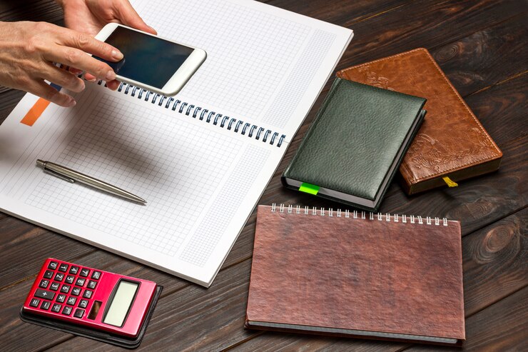 Foto manos sosteniendo autofono sobre un cuaderno abierto. calculadora y cuadernos de mesa