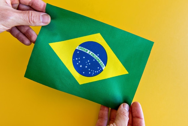 Manos sosteniendo la bandera brasileña sobre un fondo amarillo