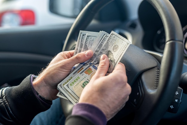 Manos sosteniendo billetes de dólar en el centro del interior del coche en el fondo del volante