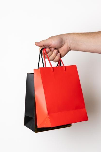Manos sosteniendo bolsas de compras rojas y negras que representan compras navideñas para Navidad o Viernes Negro