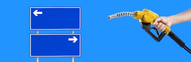 Manos sosteniendo una boquilla de combustible y un cartel de señalización azul con una flecha que indica el camino
