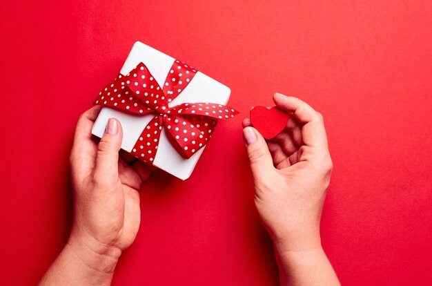 Manos sosteniendo caja de regalo con corazón pequeño sobre rojo