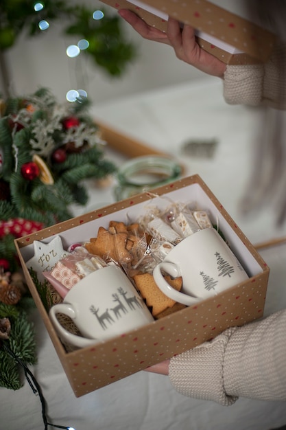 Manos sosteniendo la caja de regalo de Navidad con tazas y galletas