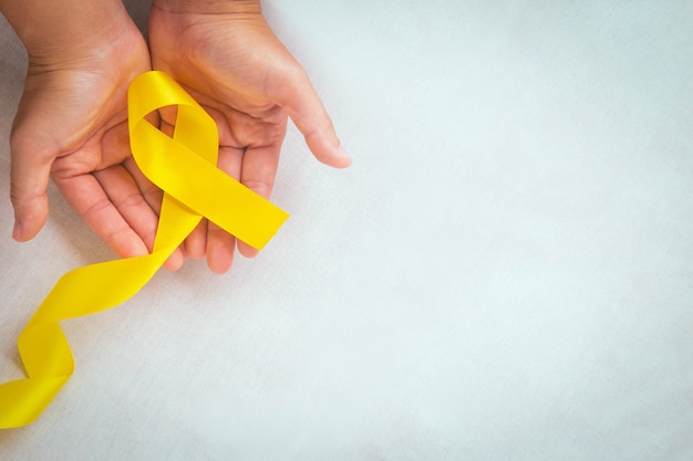 Manos sosteniendo la cinta amarilla con espacio de copia Cáncer de hueso Conciencia del sarcoma Conciencia del cáncer infantil Colangiocarcinoma Cáncer de vesícula biliar Día mundial de la prevención del suicidio Concepto de seguro de salud