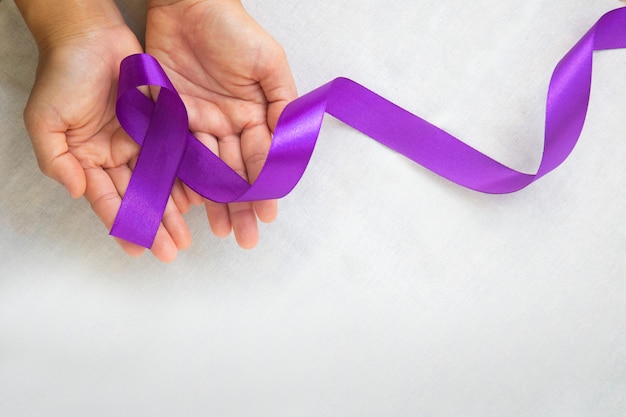 Manos sosteniendo cinta morada o violeta sobre tela blanca con espacio de copia. Cáncer de páncreas, conciencia sobre el cáncer de testículo.