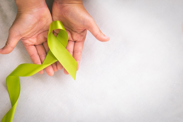 Manos sosteniendo una cinta verde lima clara sobre una mesa de tela blanca con espacio de copia Símbolo del Día Mundial de la Salud Mental y Concienciación sobre el Linfoma Concepto médico y de seguros de salud