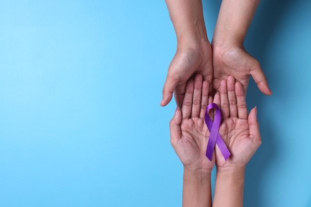 Manos sosteniendo cintas moradas día mundial contra el cáncer