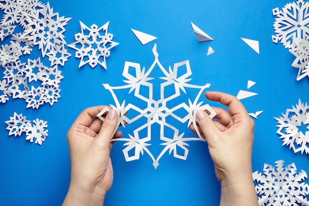 Manos sosteniendo copo de nieve de papel cortado blanco sobre superficie azul