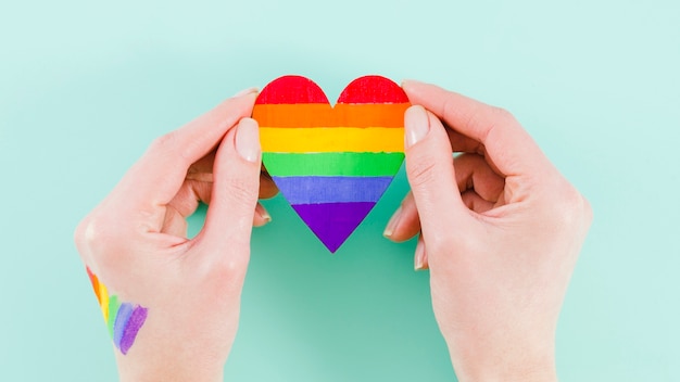 Manos sosteniendo un corazón con los colores de la bandera del día del orgullo