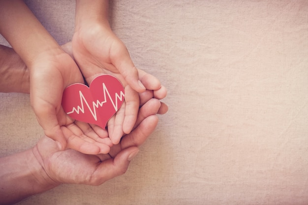 Manos sosteniendo corazón rojo con cardiograma