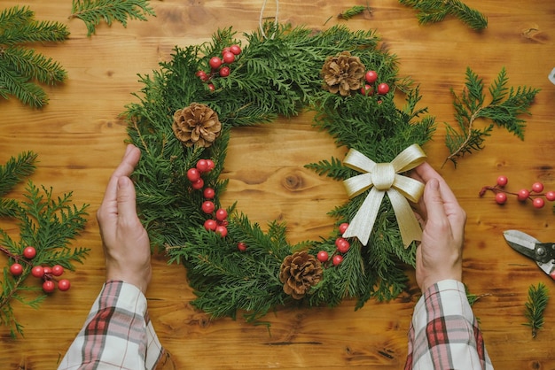 Manos sosteniendo corona de Navidad DIY decoración floral de invierno