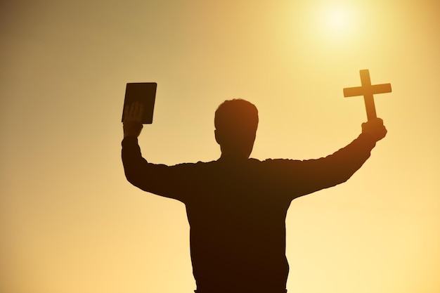 Manos sosteniendo cruz de madera y biblia