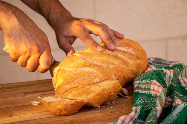 Manos sosteniendo el cuchillo y cortando el pan en rebanadas para servir