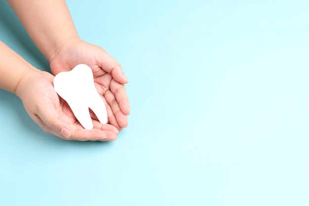 Manos sosteniendo dientes de papel en azul.