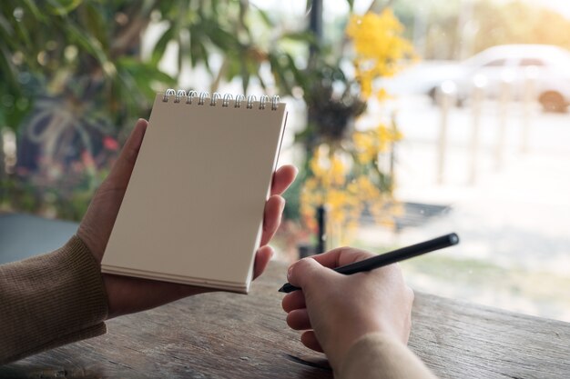 manos sosteniendo y escribiendo en un cuaderno en blanco con fondo de naturaleza borrosa