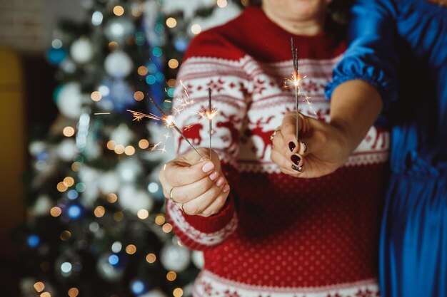Foto manos sosteniendo fuegos artificiales contra las luces de navidad en una habitación oscura feliz año nuevo vacaciones atmosféricas