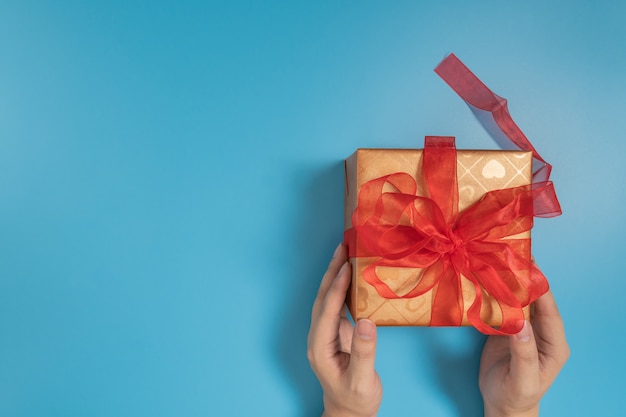 manos sosteniendo una gran caja de regalo atada con una cinta roja sobre azul