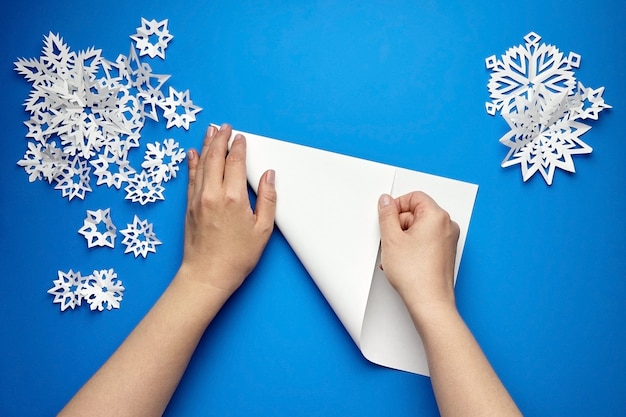 Manos sosteniendo una hoja de papel blanco para hacer copos de nieve