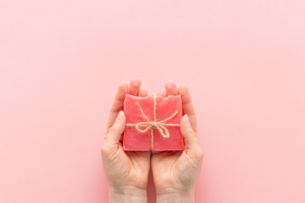 Manos sosteniendo jabón artesanal rosa sobre fondo rosa