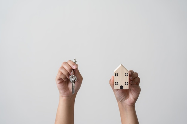 Manos sosteniendo llaves y pequeña casa de madera concepto de inversión inmobiliaria de ahorro