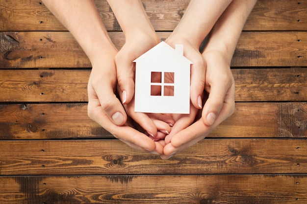 Manos sosteniendo modelo de casa sobre fondo de madera