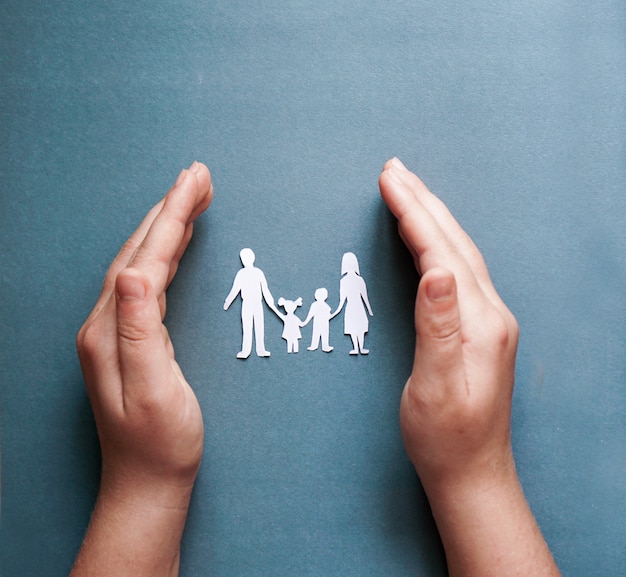 Foto manos sosteniendo recortes familiares de papel, concepto de distanciamiento social, covid19 en el fondo de color azul, protección familiar