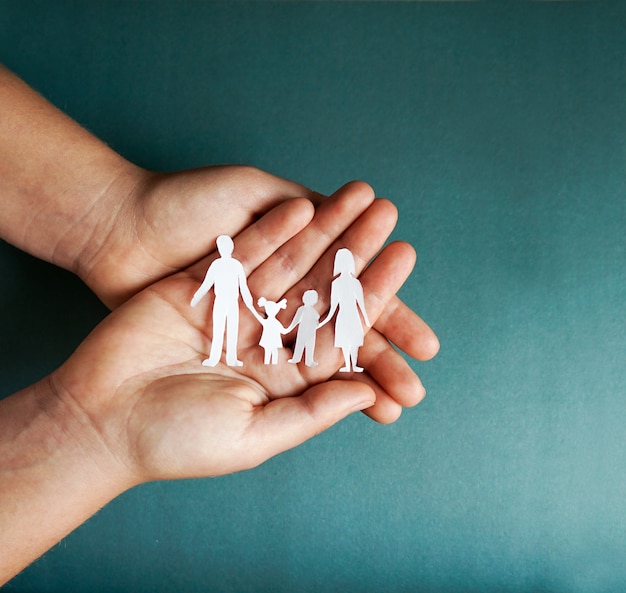 Foto manos sosteniendo recortes familiares de papel, concepto de distanciamiento social, covid19 en el fondo de color azul, protección familiar