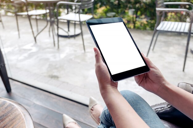 Manos sosteniendo tablet pc negro con pantalla de escritorio en blanco blanco en cafe