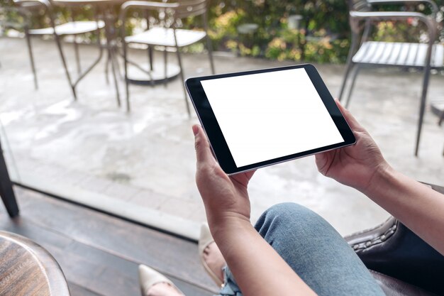 Manos sosteniendo tablet pc negro con pantalla de escritorio en blanco blanco en cafe