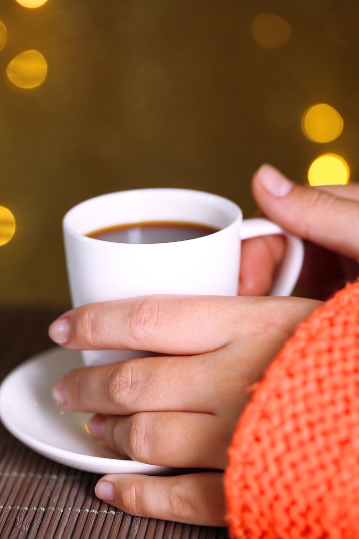 Foto manos sosteniendo la taza de bebida caliente, primer plano, sobre fondo brillante